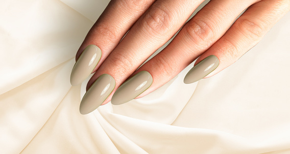 Beautiful woman brown green manicure on creative trendy brown green background with silk fabric. Minimalist manicure trend