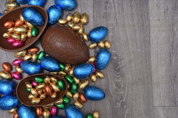 istock Pile or group of multi colored and different sizes of colourful foil wrapped chocolate easter eggs in pink, blue, gold and green. Large halves of a brown milk chocolate egg have mini eggs inside, on a grey wooden background. 1465357811