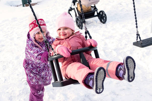 zwei freundinnen 3-5 jahre alt schaukeln auf einer schaukel in einem winterpark, auf einem spielplatz. die freude an der freundschaft. - child winter snow 4 5 years stock-fotos und bilder