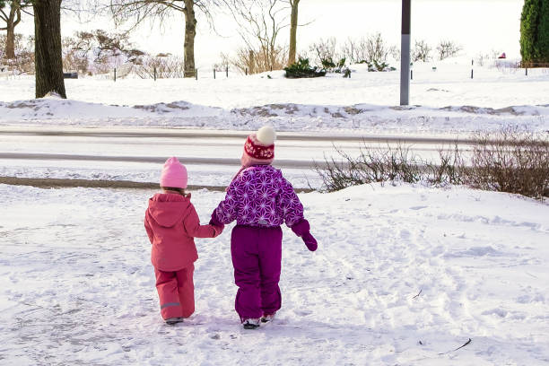 zwei kaukasische mädchen im alter von 3-5 jahren laufen in richtung stadtstraße. winterspaziergang. - child winter snow 4 5 years stock-fotos und bilder