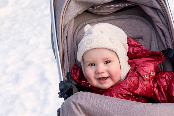 A one-year-old baby, a Caucasian boy, lies in a baby carriage and smiles. Walk in the winter in the park A one-year-old baby, a Caucasian boy, lies in a baby carriage and smiles. Walk in the winter in the park baby stroller winter stock pictures, royalty-free photos & images
