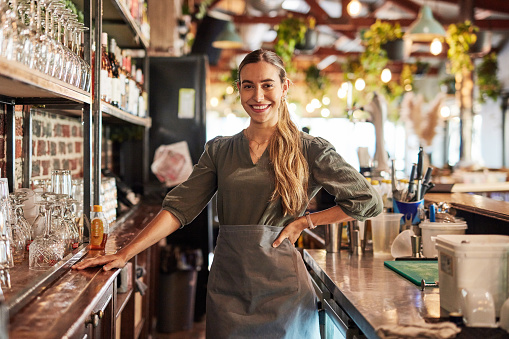 Portrait of woman, bartender or pub owner with smile at counter, hospitality startup investment in alcohol sales. Success, confidence and small business, service industry manager at bespoke wine bar.