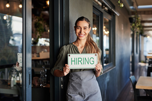 Coffee shop, hiring and sign with a woman small business owner standing outside of her cafe for recruitment. Portrait, vacancy and a job in the hospitality industry with a female entrepreneur outside
