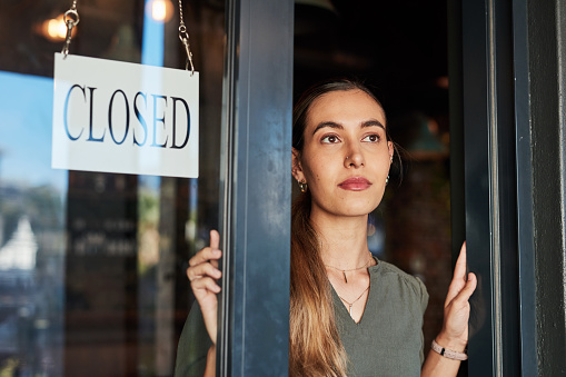 Closed shop sign, woman thinking and female business owner at a cafe or restaurant. Young person, entrepreneur and employee closing coffee place with poster and bulletin of bankruptcy from debt