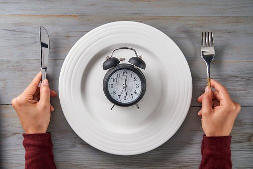 Time themes: Time to eat. Top view of woman hands with cutlery and a clock on a plate
