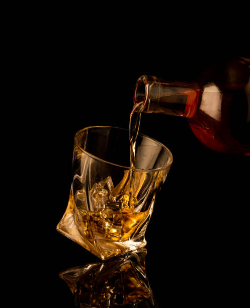 istock Pouring alcohol and throwing an ice cube into a glass with splashes on a black background 1465371877