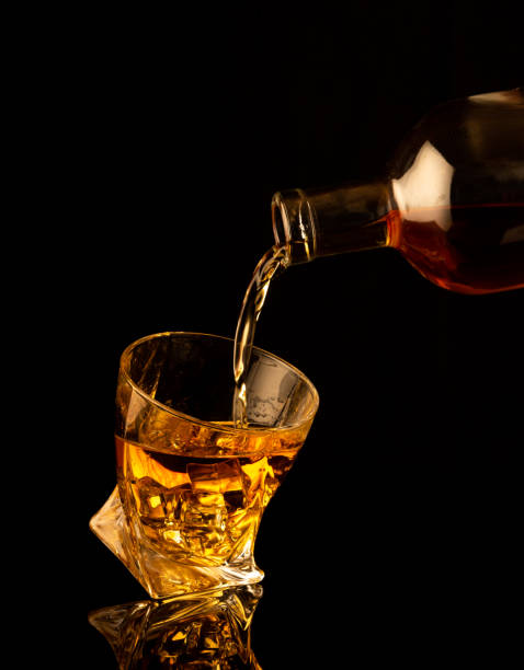 アルコールを注ぎ、黒い背景に水しぶきのあるグラスに角氷を投げる - whisky glass ice cube alcohol ストックフォトと画像