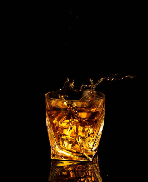 アルコールを注ぎ、黒い背景に水しぶきのあるグラスに角氷を投げる - whisky glass ice cube alcohol ストックフォトと画像