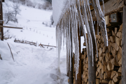 Icicles hanging from the snowy roof of a mountain hut and stacks of wood