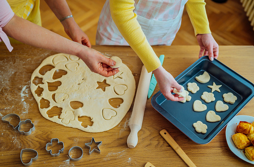 Cheerful mother and daughter preparing cookies with cookie cutter in kitchen