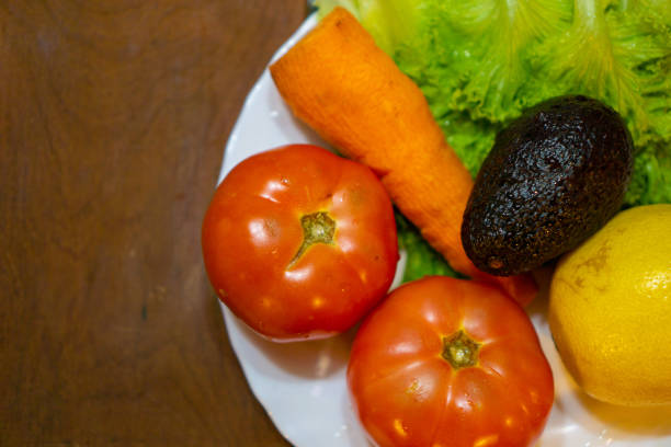 Closeup of a group of healthy fruit, milk, and vegetables sitting on a green grass background. The imperfect, realistic produce consists of mushrooms, peas, lettuce, pepper, blueberries, strawberries, lemons, squash, and avocado.