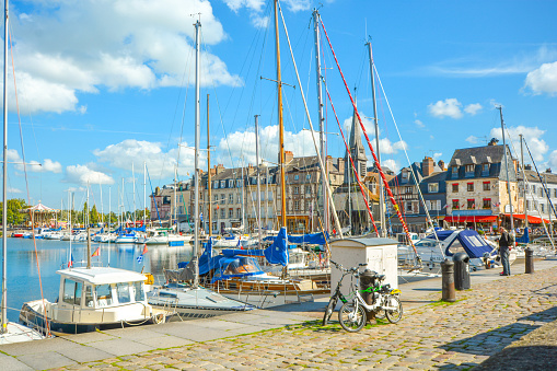 Boats, yachts and fishing vessels line the old harbor or Vieux Bassin in the charming Normandy village of Honfleur, France, with cafes and shops surrounding the marina. Honfleur is a city in the department of Calvados, in northern France's Normandy region. It's on the estuary where the Seine river meets the English Channel. The Vieux-Bassin (old harbor), lined with 16th- to 18th-century townhouses, has been a subject for artists including Claude Monet and native son Eugène Boudin.
