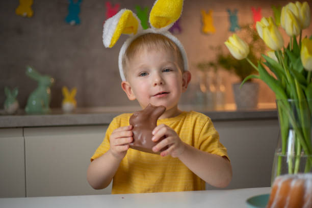 istock A cute little boy wearing bunny ears on Easter day is eating a chocolate Easter bunny. A child plays egg hunt for Easter. Charming child celebrates Easter at home 1465388472