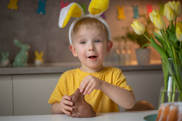 istock A cute little boy wearing bunny ears on Easter day is eating a chocolate Easter bunny. A child plays egg hunt for Easter. Charming child celebrates Easter at home 1465388504