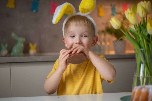 istock A cute little boy wearing bunny ears on Easter day is eating a chocolate Easter bunny. A child plays egg hunt for Easter. Charming child celebrates Easter at home 1465388514