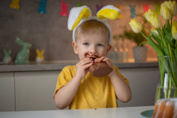 istock A cute little boy wearing bunny ears on Easter day is eating a chocolate Easter bunny. A child plays egg hunt for Easter. Charming child celebrates Easter at home 1465388562