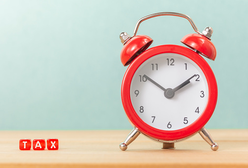 Tax Time concept. TAX word and Red Alarm Clock on wooden table.