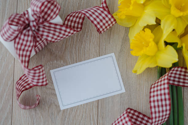 Directly above of empty letter surrounded by gift box with big ribbon and a bouquet of yellow flowers for special occasion.