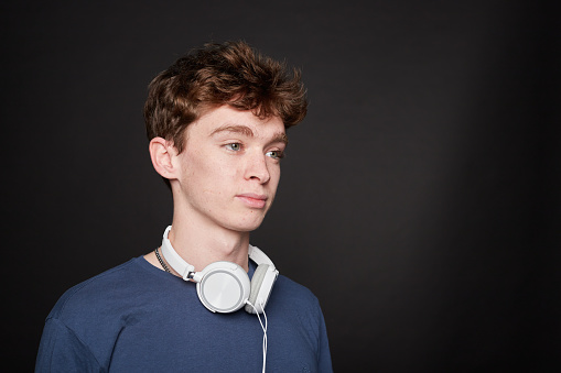 Side view of a young man putting on headphones in a photo studio with a gray background