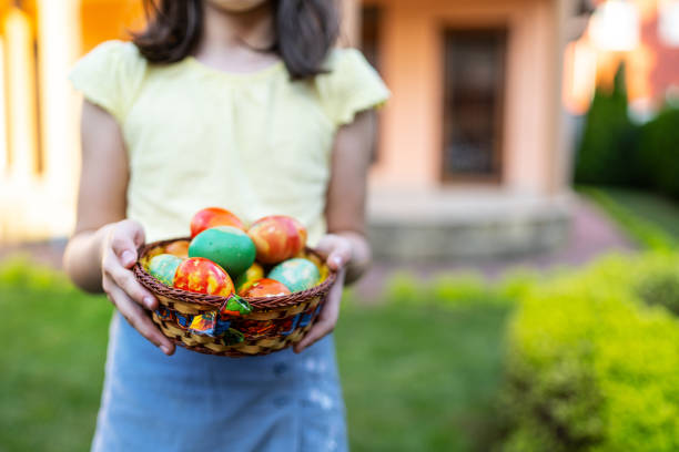 A young unknown girl is standing outside on a sunny day holding an Easter basket filled with chocolate eggs