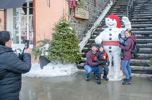 Woman taking a picture of family with Bonhomme Carnaval statue during winter day in Quebec city