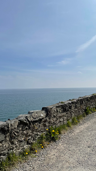 A rocky footpath running along the blue waters of the Irish Sea on a clear summer day in Co. Wicklow, Ireland