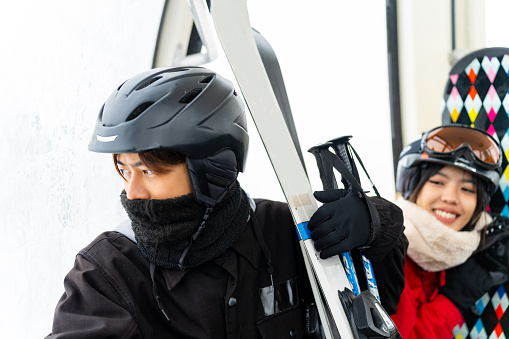 Asian couple rises to snowy mountain peak on cableway cabin
practicing snowboard and ski at ski resort. Man and woman enjoy outdoor active lifestyle winter extreme sport training on holiday vacation.