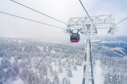 Point of view cableway moving up to snowy mountain peak ski resort. \nAerial view of pine tree forest mountain covered in snow under cable car. Ski lift transportation and winter travel vacation concept