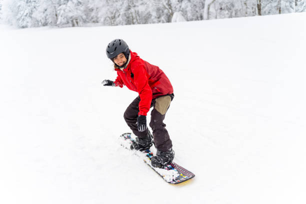 Asian woman snowboarding on snowy mountain at in ski resort. Young Asian woman practicing snowboard on snowy mountain slope at ski resort. Attractive girl enjoy outdoor active lifestyle extreme sport training freeride snowboarding on winter holiday vacation. japanese snowboarder stock pictures, royalty-free photos & images