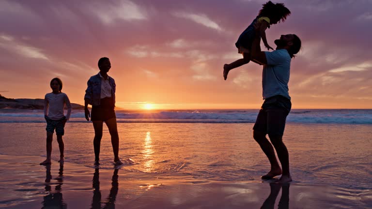 Family, sunset and children on beach playing with couple walking in sand and waves in silhouette in Hawaii. Travel, summer evening ocean and kids with woman and man, fun on tropical island holiday.