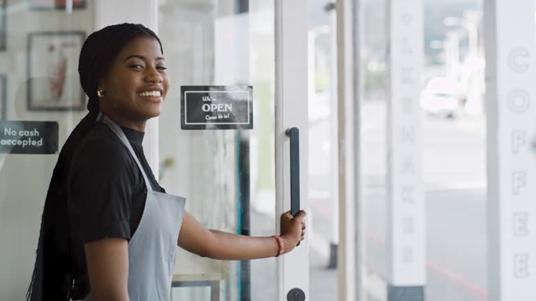 Small business, coffee shop and black woman open door of restaurant or cafe. Smile of entrepreneur, waitress or manager person ready to welcome for hospitality service at store or entrance or startup