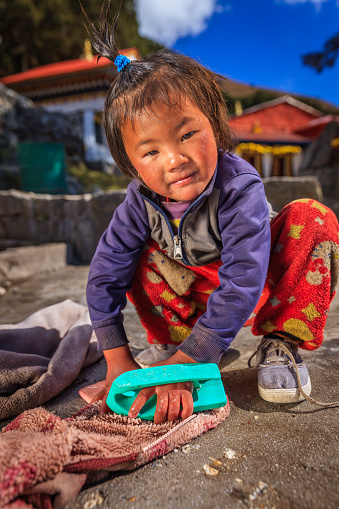 Little Sherpa girl washing clothes in the her village, Buddhist monastery on the background, Mount Everest National Park, Nepal. This is the highest national park in the world, with the entire park located above 3,000 m ( 9,700 ft). This park includes three peaks higher than 8,000 m, including Mt Everest. Therefore, most of the park area is very rugged and steep, with its terrain cut by deep rivers and glaciers.