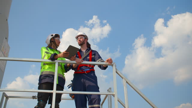 Two survey engineers talking at the base of a wind turbine stand.