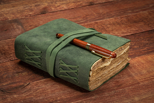 retro leather-bound journal with decked edge handmade paper pages with a stylish pen on a rustic barn wood table, journaling concept