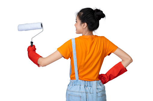 Rear view of an Asian young housewife in a protective glove holding a roller paint brush isolated over white background