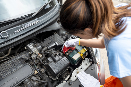 Asian woman car technician in uniform checking car engine on the road