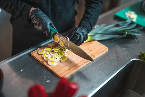 Female hands cutting leek. She is using gloves, and is focused on creating a delicious Asian meal from scratch.