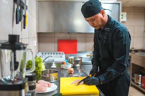 Indoor shot of an Indonesian cook showcasing his culinary skills. He is cutting ingredients with ease in the restaurant kitchen.