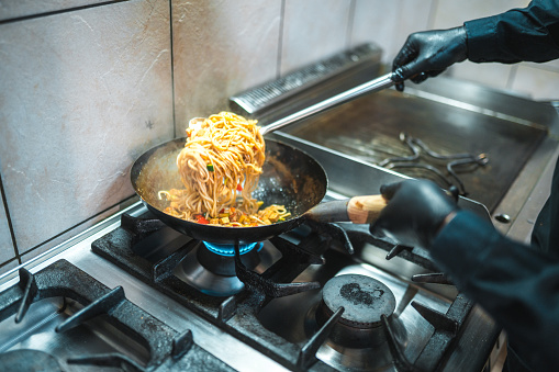 Male hands cooking stir fry noodles. Delicious noodles are combined with vegetables and soy sauce.