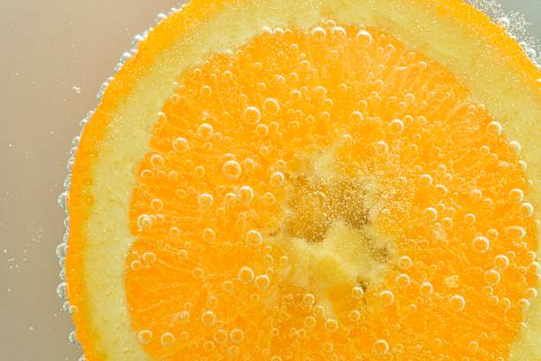 Slice of orange fruit in water on white background. Orange close-up in liquid with bubbles. Slice of red ripe orange in water. Macro image of fruit in water stock photo