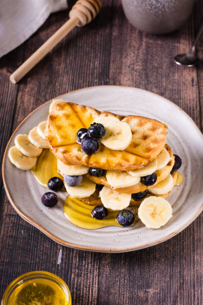 A stack of waffles with banana, blueberries and honey on a plate. Comfort food. Vertical view
