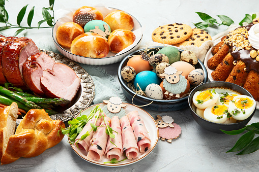 Classic Easter ham dinner. Top view table scene on a white background. Ham, eggs, hot cross buns, carrot, cake and vegetables.