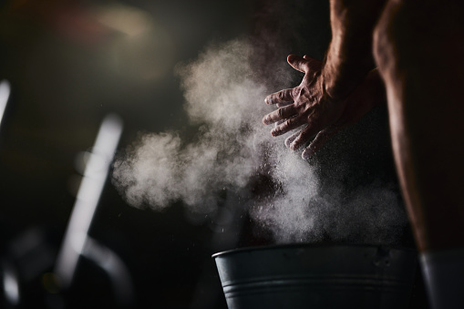 Close up of unrecognizable male athlete clapping his hands with powder while preparing for sports training in a gym.