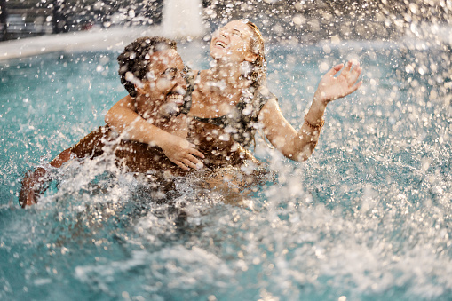 A young beautiful woman making water splash at the pool, enjoying summer. Summer vacation concept.