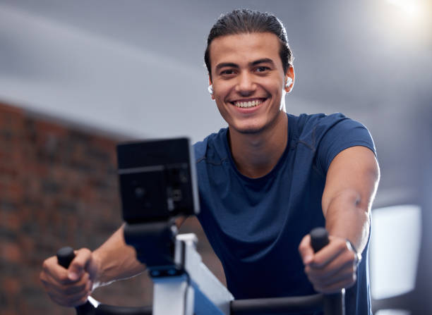 運動、トレーニング、または健康的な有酸素運動トレーニングのためのジムでの男性、フィットネス、サイクリング。ポートレート、幸せな笑顔、または健康、ウェルネス、または持久力ス� - フィットネスマシン ストックフォトと画像