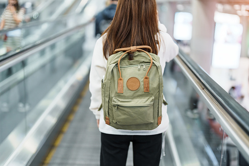 Asian woman traveler with backpack walking on escalator  in international airport. time to Travel, Vacation, trip and Transport concept