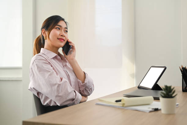 istock Confident female investment advisor talking on mobile phone with client and using digital tablet at her workstation. 1465469441