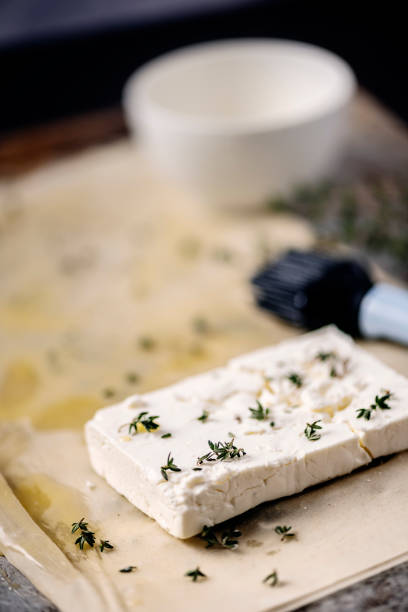 Making feta cheese wrapped in filo pastry. Take one sheet of filo pastry and brush it with melted butter and sprinkle some fresh thyme over it, fold it in half and spread  more butter and thyme over the pastry. Place your feta cheese on the pastry, add more thyme to it and prepare to wrap the cheese in the filo pastry.  Colour, vertical format with some copy space.