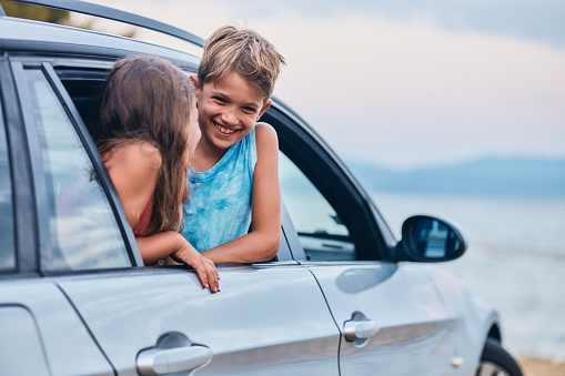 Beautiful boy and girl enjoying summer vacation traveling by car by the beach.