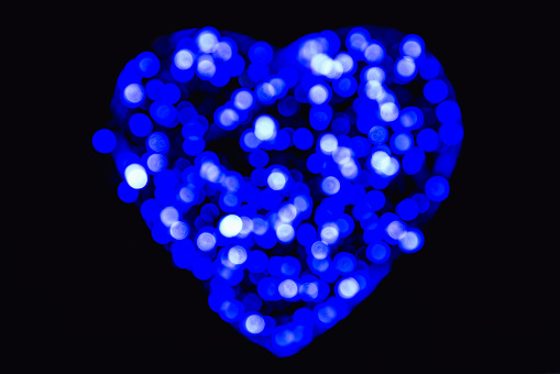 Blue and white defocused bokeh circles of light in the shape of a heart on a black backdrop (background for Valentines Day)